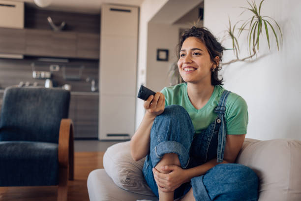 Young woman sitting on the sofa, watching TV at home and enjoying.